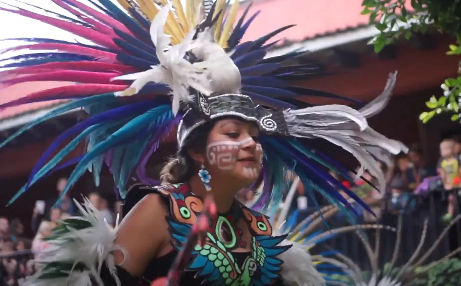 A dancer in a vivid blue and pink feathered headdress performing at the Family Adventure Summit